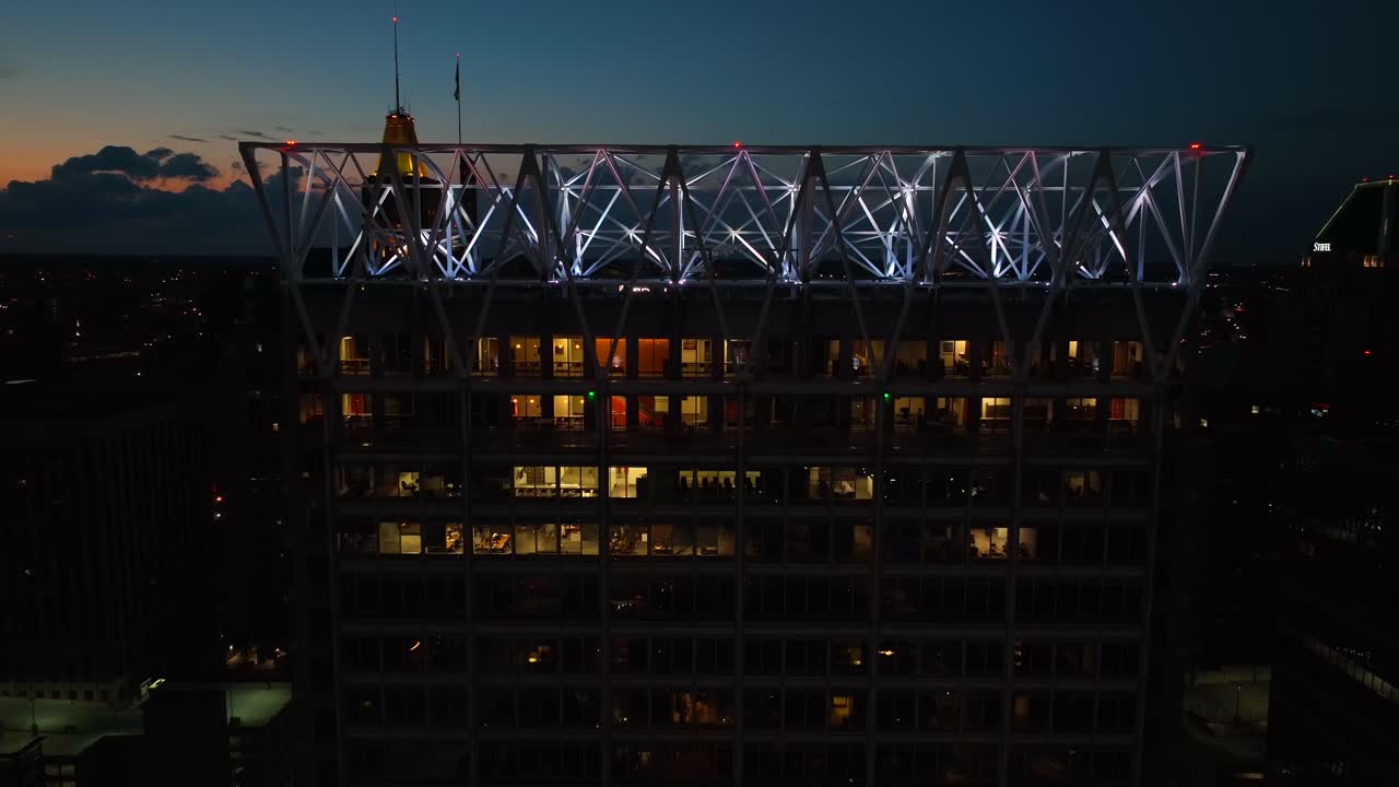 Highrise skyscraper tower at night in American city. Office building with lights on. Descending aerial
