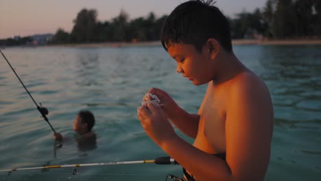 two boys fishing in the ocean at sunset