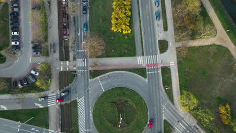 overhead view of a roundabout intersection with vehicles in motion, surrounded by pedestrian crosswalks and patches of green