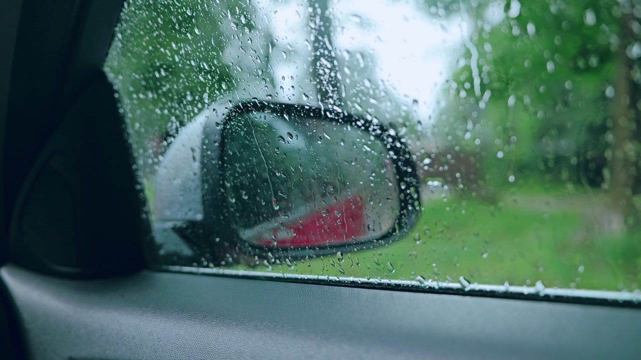 Fotogramma statico di un finestrino d'auto piovoso con gocce d'acqua e riflesso a specchio