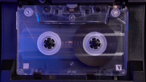 transparent audio cassette tape playing from start in vintage deck player, close up