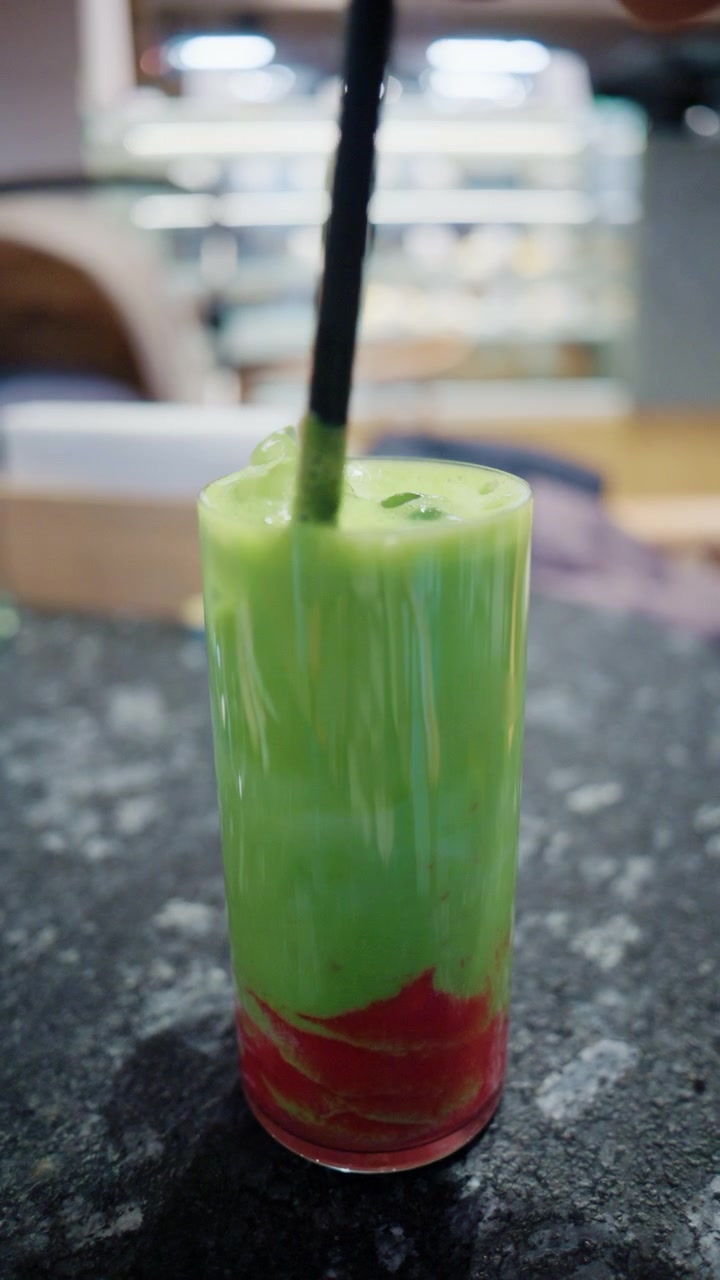 Primo piano di una bevanda verde colorata con una cannuccia nera su un tavolo da caffè.