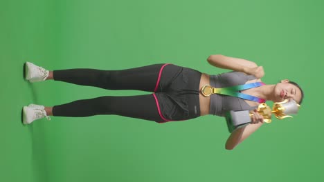 cuerpo lleno de mujer asiática con una medalla de oro mirando un trofeo de oro luego celebrando la victoria como el primer ganador en el fondo de la pantalla verde en el estudio