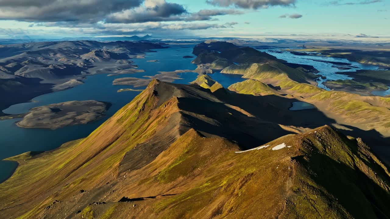 A sweeping aerial view of Iceland’s layered highlands, revealing fractured ridges, island-dotted lakes and vast volcanic plains in a clean, documentary - style overview