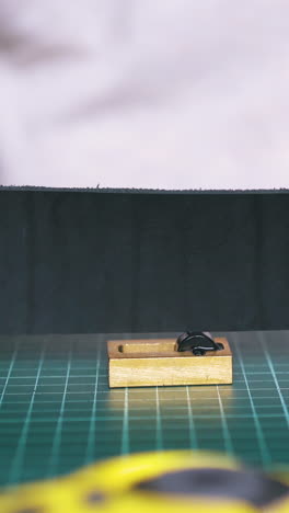 cu: skilled woman tailor colours leather strip edges with black paint using pure copper in workshop close view
