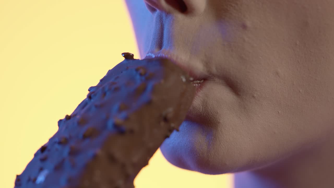 mujer tomando un bocado de helado de chocolate en primer plano, fondo amarillo