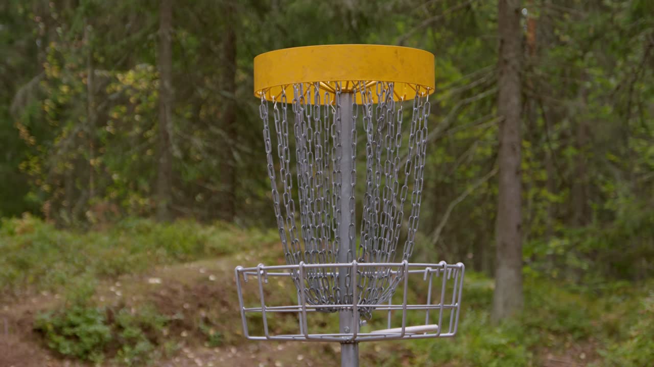 Disco da disc golf che vola nel cesto nella foresta - ripresa completa al rallentatore del cesto.