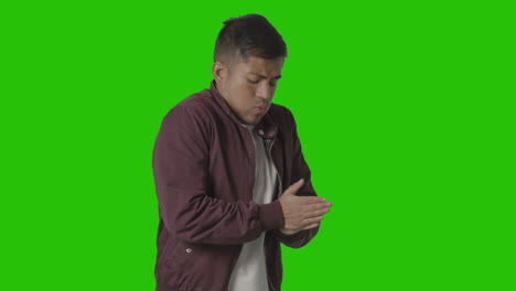 portrait of cold shivering casually dressed young man doing up coat against green screen 1