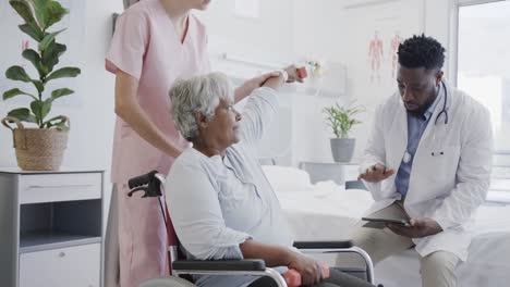 diverse male doctor and female physio treating senior female patient in wheelchair, slow motion