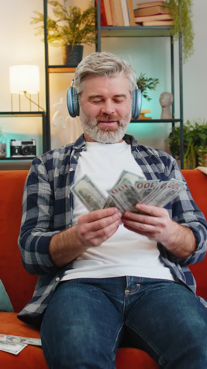 Blije, vrolijke Kaukasische senior man met draadloze hoofdtelefoon die geld laat rollen en smijt