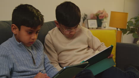 two young boys sitting on sofa at home playing games or streaming onto digital tablets 8