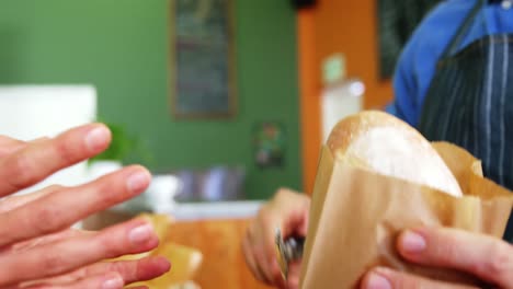 Mid-section-of-woman-purchasing-bread-at-bakery-store