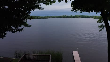 Slow-aerial-shot-gliding-through-trees-above-boat-dock-on-lake