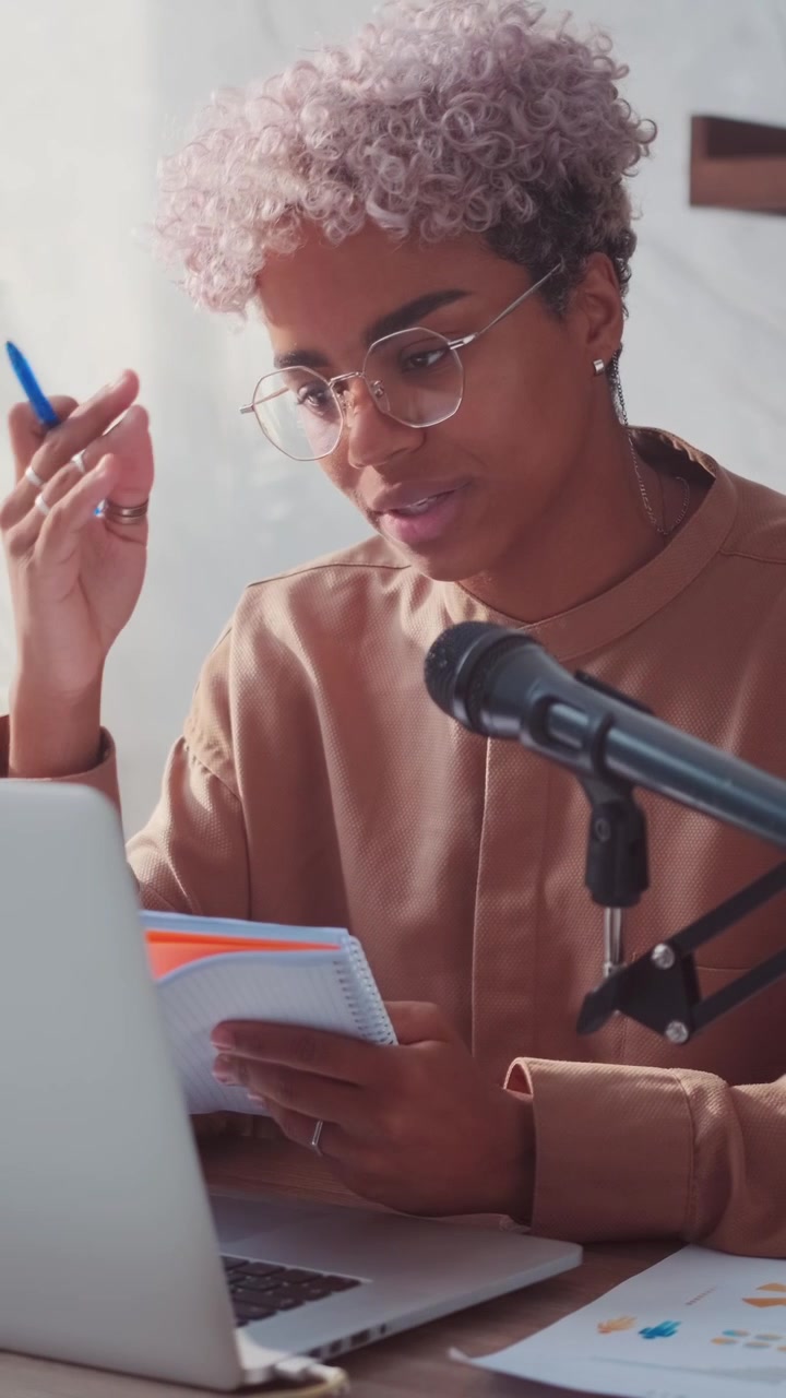 Joven mujer afroamericana concentrada tomando notas durante la grabación de un podcast.