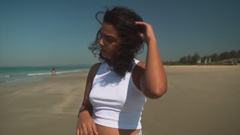 Girl-on-the-beach,-fixing-her-hairs-as-the-wind-blows-over-the-sand-and-waves