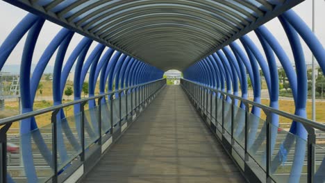 crossing a bridge over the highway made of blue metal tubes on foot