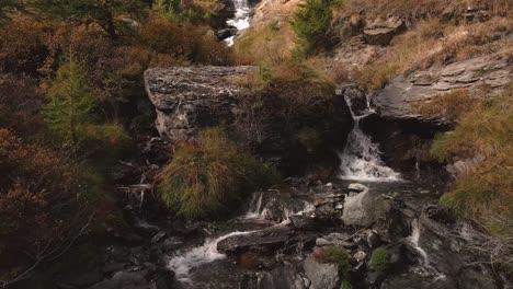 cascades flowing over rocky valley with autumn forest in piemonte, italy