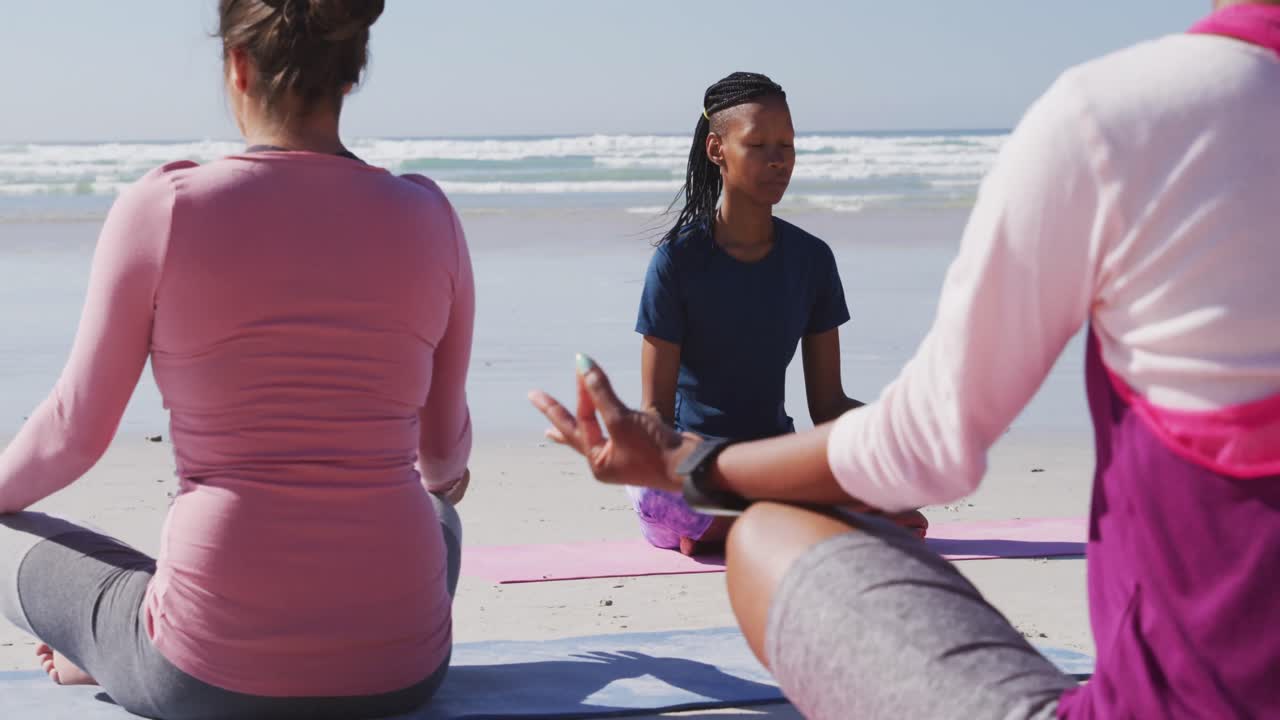 grupo multiétnico de mujeres haciendo yoga en la playa y fondo de cielo azul