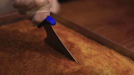 pastry chef carefully cuts with a knife into the slices of kadaifi baked dessert in the large baking tray