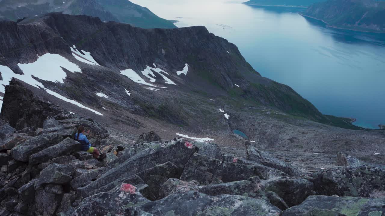 A Lady Reclining on the Mountain's Summit Rocks in Kvænan, Norway - Aerial Pan Right