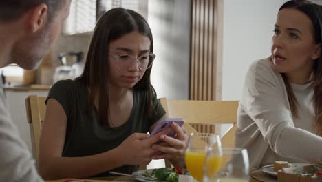 Teenage-girl-using-mobile-phone-during-breakfast-at-the-table