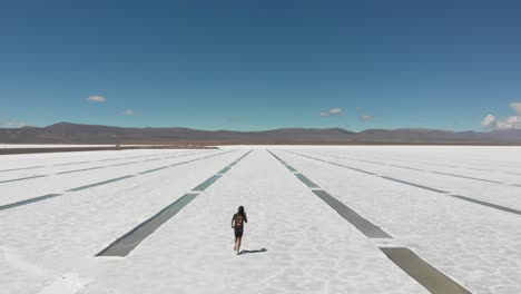 aerial of a lone figure runinng along the extraction pits of the salt flats of salinas grandes, argentina