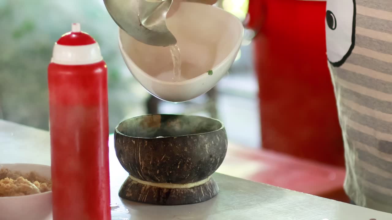 el vendedor sirve sopa de fideos en la cáscara de coco