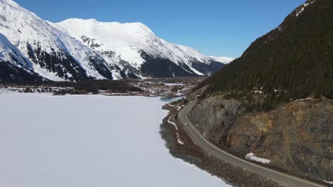 Luftaufnahme-Einer-Drohne,-Die-Um-Die-Seite-Eines-Berges-Herumschwenkt,-Der-Mit-Kiefern-Bedeckt-Ist,-Und-Blick-Auf-Schneebedeckte-Berge-In-Alaska