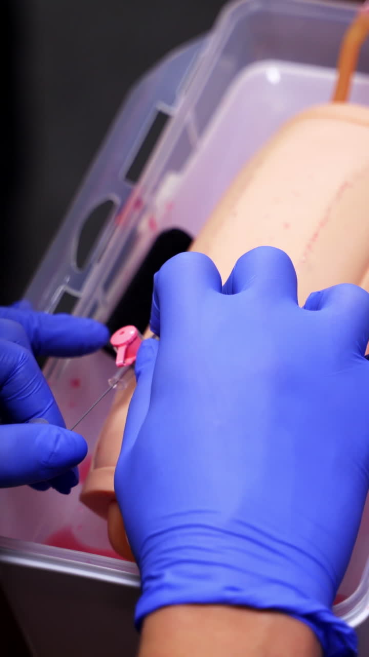 Catheter insertion learning. Students in sterile gloves study to put a catheter on a dummy hand. Medical training. Close-up. Vertical video