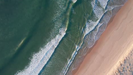 foamy ocean waves hitting sandy beach, aerial top down view