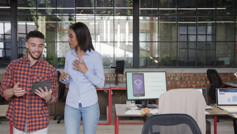 Happy-diverse-male-and-female-colleagues-using-tablet-and-walking-through-office-talking,-copy-space