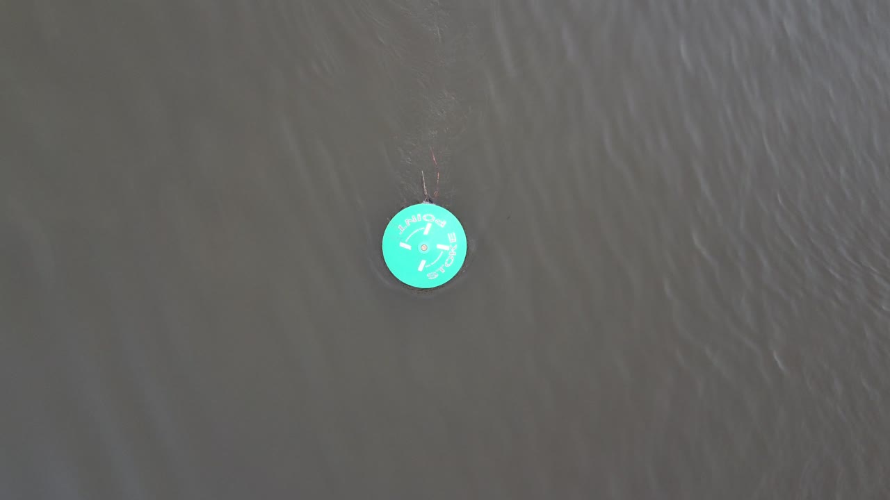 A top down drone shot of a green navigation buoy with the tide streaming past