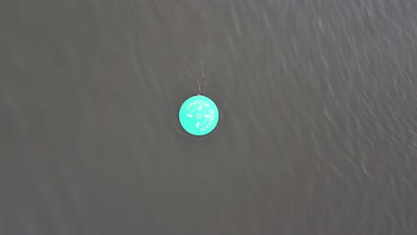A top down drone shot of a green navigation buoy with the tide streaming past