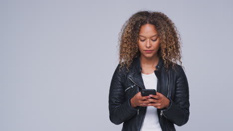 Studio-Shot-Of-Woman-Wearing-Leather-Jacket-Sending-Text-Message-On-Mobile-Phone-In-Slow-Motion