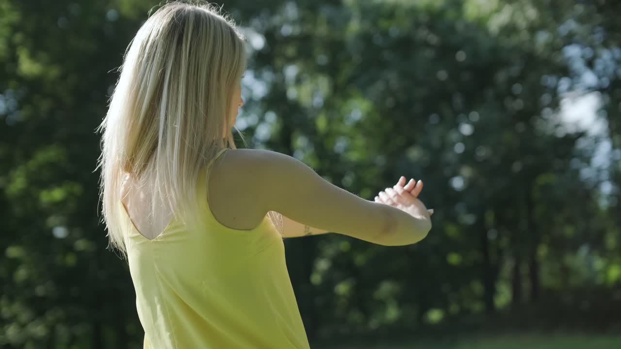 Kvinde i gul kjole danser ved træ i sommerpark