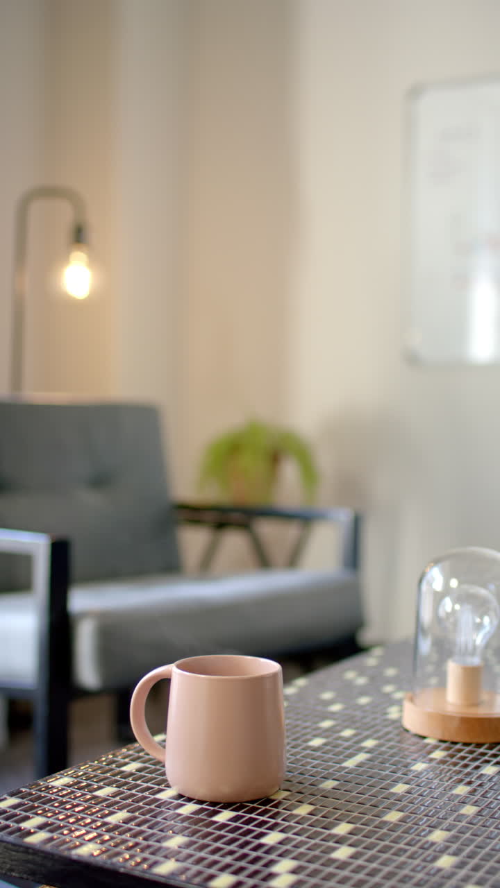 Vertical video: Pink coffee mug on office table with chair and lamp in background