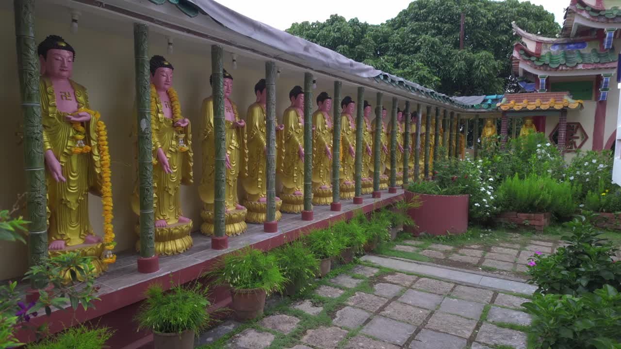 A serene garden walkway at Kek Lok Si Temple lined with a row of golden Buddha statues, surrounded by lush greenery and traditional Chinese architecture.