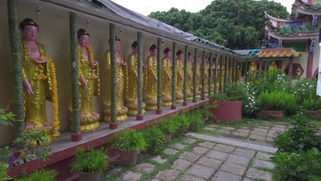 a serene garden walkway at kek lok si temple lined with a row of golden buddha statues, surrounded by lush greenery and traditional chinese architecture.