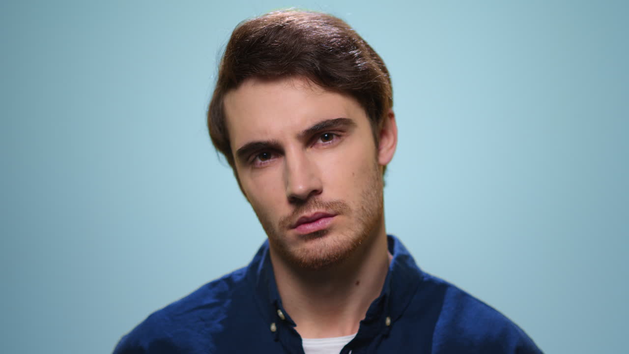 Serious man standing on blue background. Pensive guy looking at camera in studio