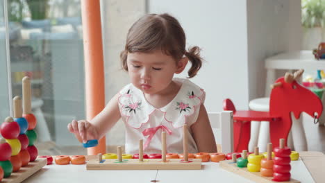 adorable blond toddler girl stacking colorful rings on poles sitting at playground room for children - child early education