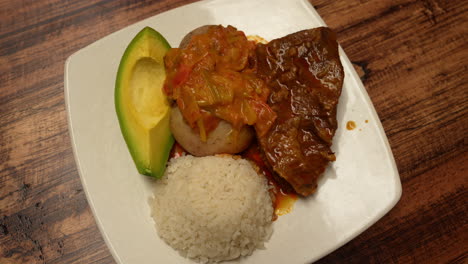 close-up shot of a colombian classic sobrebarriga, beautifully plated with white rice and fresh avocado on a rustic wooden table. rich colors and inviting textures enhance the culinary appeal