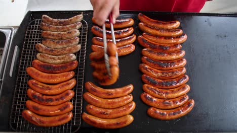 hombre volviendo salchichas y enlaces calientes en una parrilla plana en el sur fuera de un restaurante y camión de comida para la cena de verano o el almuerzo chisporroteando perritos calientes