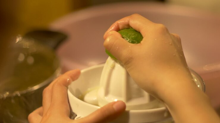Green lime being juice using electric citrus juicer, filmed over right shoulder as close up shot