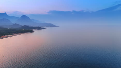 blue and pink waterscape of the sea merging with cloudscape in the sky. mountains silhouettes in the fog at sunset. aerial view