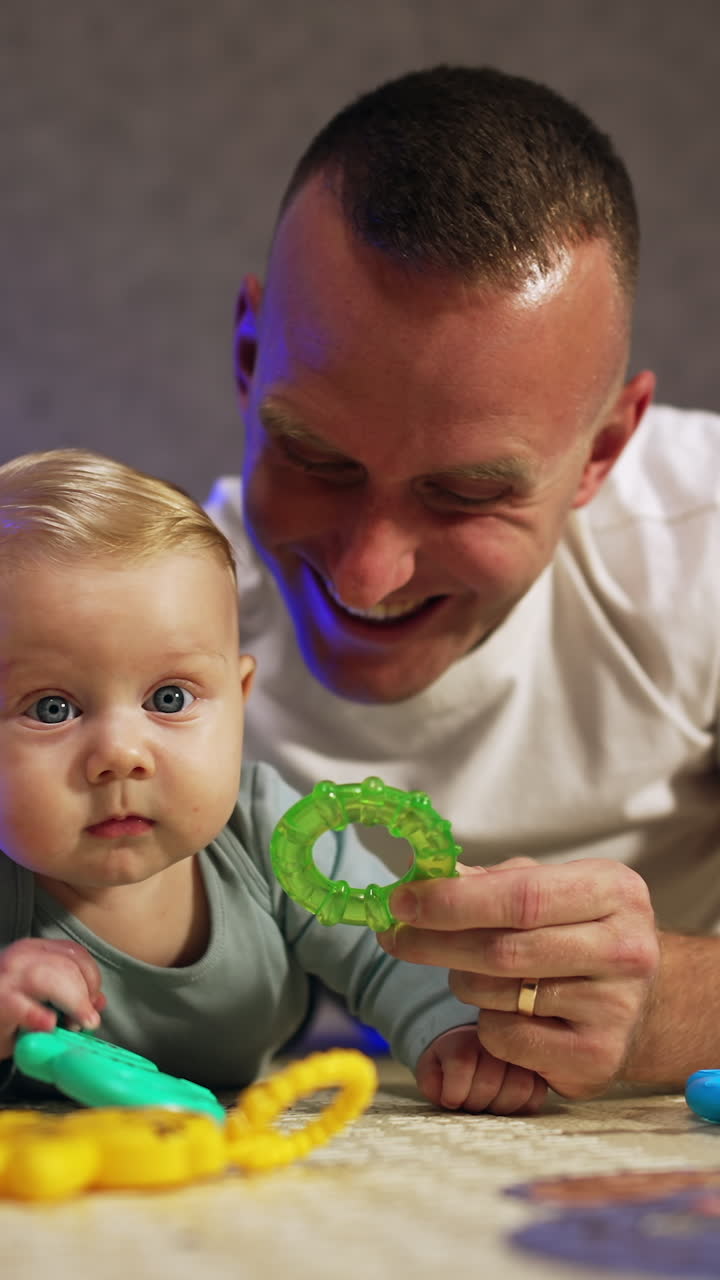 Padre e figlio neonato che passano del tempo insieme a casa. Uomo con un bambino sdraiato sul pavimento che dà giocattoli al figlio. Primo piano. Video verticale