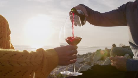 man pouring wine for woman by the sea