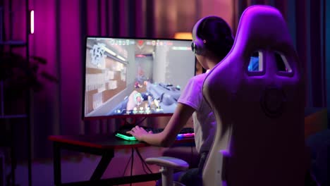 una adolescente asiática emocionada celebra la victoria mientras juega a videojuegos en la computadora, videojuegos de disparos en línea