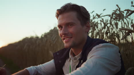 Smiling-farmer-posing-at-wheat-field-portrait.-Tired-worker-resting-at-sunset.