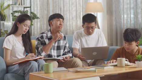 asian teen group studying at home. helping each other doing project, a girl writing into notebook, a boy in plaid shirt thinking, a boy in white t-shirt typing on laptop sitting next to another boy reading