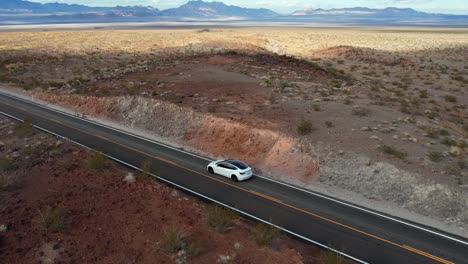antena cinematográfica de un coche eléctrico blanco y moderno que se conduce por sí mismo en una carretera desértica vacía rodeada de montañas